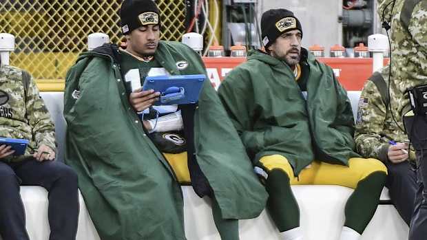 Jordan Love and Aaron Rodgers sit on the sidelines in a Packers game.