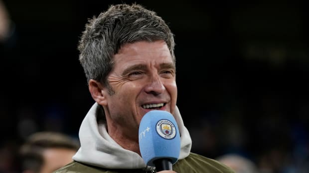 Musician and Manchester City fan Noel Gallagher speaks into a microphone with the club’s logo on it.
