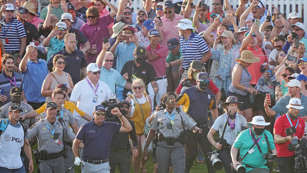 Phil Mickelson walks toward the 18th green at the PGA Championship, fist raised, with a throng of fans behind him.