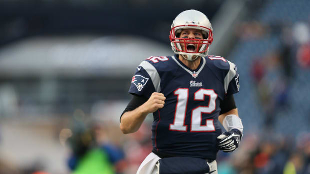 Tom Brady yells with a clenched fist in celebration, wearing a Patriots jersey and helmet