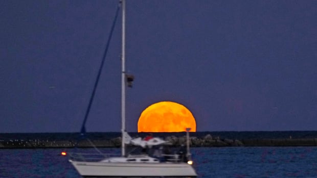 A sailboat passes by a full supermoon, called the Buck Moon, as it rises over Lake Michigan in Milwaukee on Wednesday, July 13, 2022.