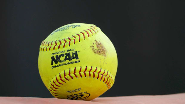 A yellow NCAA softball sits on a dugout during a game.