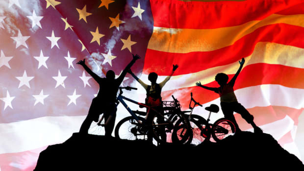 Silhouette of a family next to bicycles in front of a large American flag