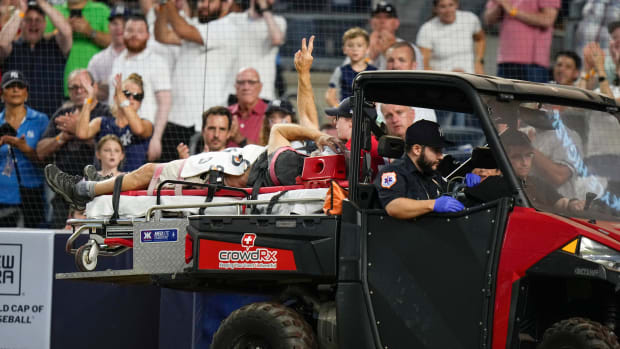 A camera operator who was injured on a throwing error holds up his right hand to the crowd as he is carted off the field.