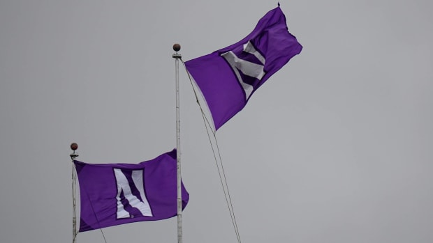 Two Northwestern flags fly in a gray sky during a football game.