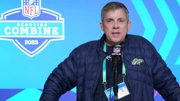 broncos head coach Sean Payton stands at a microphone talking with a NFL scouting combine logo on the wall behind him