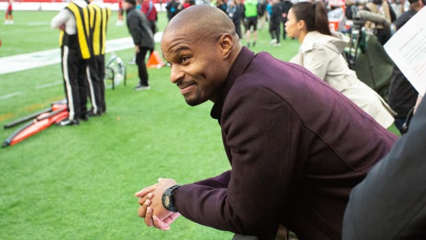 Osi Umenyiora smiles and leans in from the first row of the stands at a 2019 NFL game in London