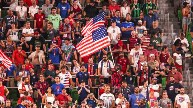 Two U.S. soccer fans hold up American flags at a United States Men's National Team soccer match.