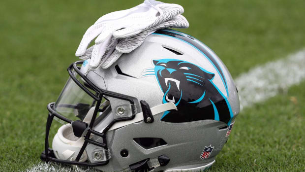 Two gloves on top of a Panthers helmet that is sitting on a field.