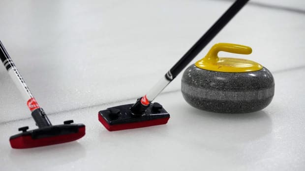 Two Curling brooms and a Curling stone sit on the ice before a match.
