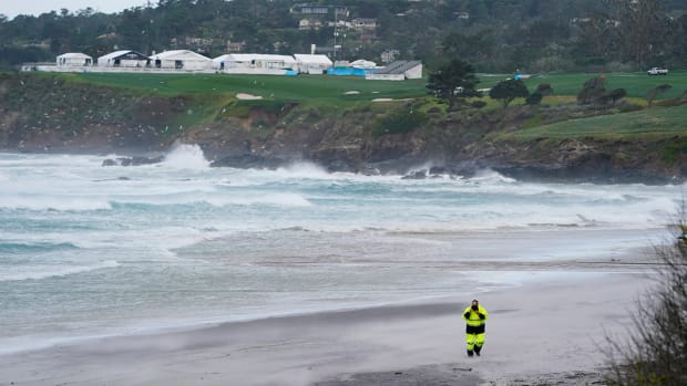 A person walks on the beach below the course as waves crash and tents blow in the wind along the eighth fairway during the postponed final round of the AT&T Pebble Beach Pro-Am golf tournament at Pebble Beach Golf Links. 