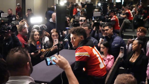 Patrick Mahomes sits at a table with a microphone surrounded by reporters and cameras