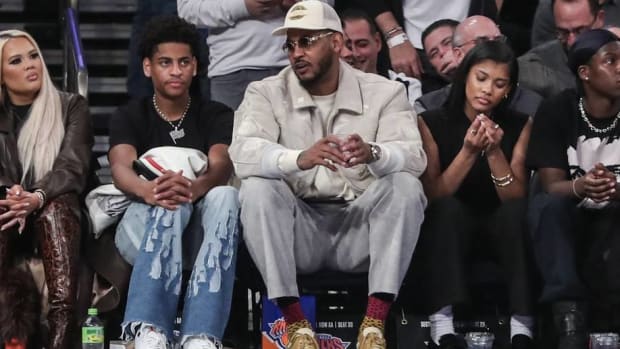 Carmelo Anthony and his son, Kiyan, watch a basketball game from the sidelines.