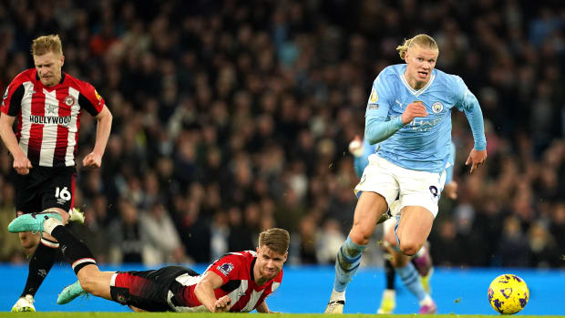Manchester City striker Erling Haaland pictured (right) running with the ball following a slip  by Brentford defender Kristoffer Ajer (center) during a Premier League game at the Etihad Stadium in February 2024
