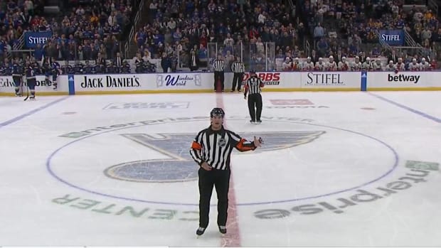 NHL referee Garrett Rank announces a replay review decision during a St. Louis Blues game.