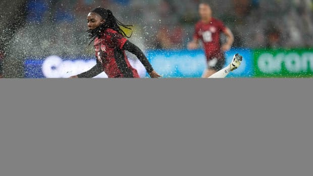 A USWNT player falls to the ground as water splashes up from the grass