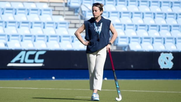 UNC field hockey coach Erin Matson stands with a field hockey stick while watching her team practice.
