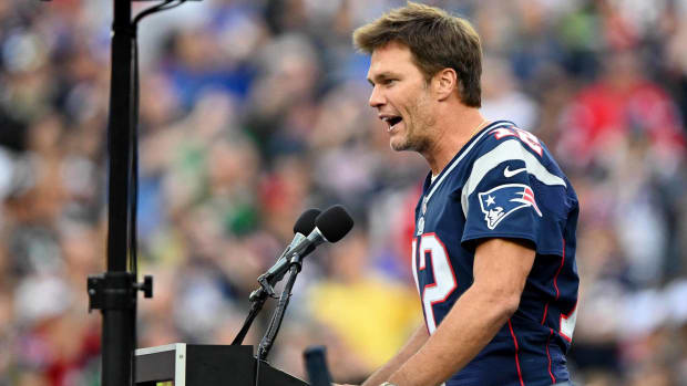 Former Patriots quarterback Tom Brady speaks to the New England crowd at a podium while being honored at halftime of a game.