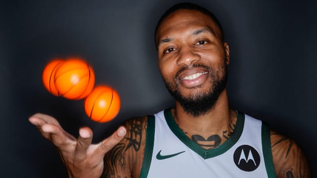 Damian Lillard throws up three mini basketballs while smiling for a picture at Bucks media day