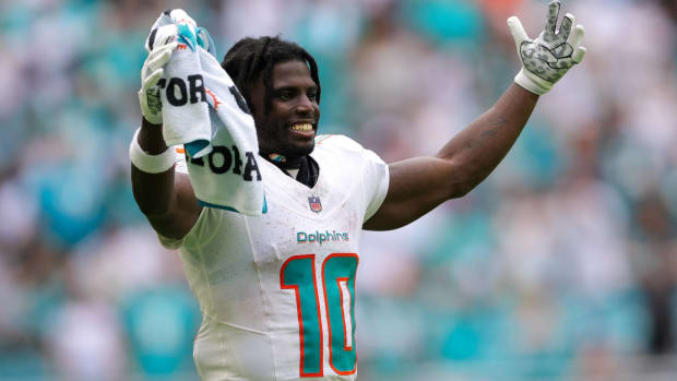 Dolphins wide receiver Tyreek Hill holds his hands up in celebration on the sidelines of a game.