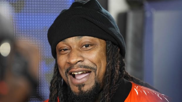 Former NFL running back Marshawn Lynch smiles while being interviewed at a college football game.