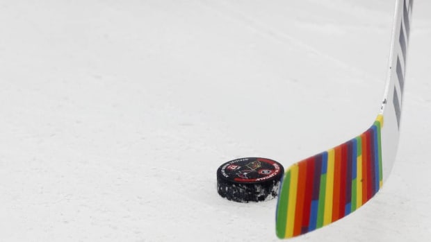A hockey stick with rainbow Pride tape on the ice next to a puck.
