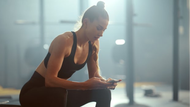 A seated woman looks at her mobile device inside of a gym