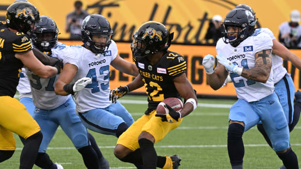Sep 5, 2022; Hamilton, Ontario, CAN; Hamilton Tiger-Cats slotback Tim White (12) runs with the ball against Toronto Argonauts linebacker Trevor Hoyte (43) and defensive back Daniele Adeboboye (21) in the first half of the annual Labor Day Classic at Tim Hortons Field. Mandatory Credit: Dan Hamilton-USA TODAY Sports