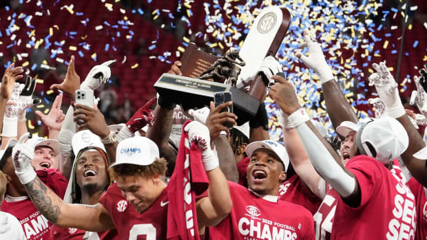 Alabama football players celebrate winning the 2023 SEC championship over Georgia by hoisting a trophy.