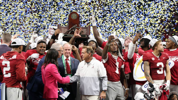 Nick Saban shakes a woman’s hand as his players stand behind him and hold up the SEC Championship trophy