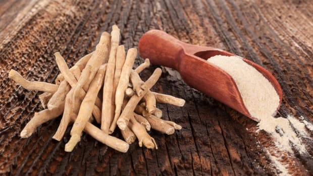 A wooden background featuring a pile of ashwagandha root next to a scoop of ground ashwagandha powder