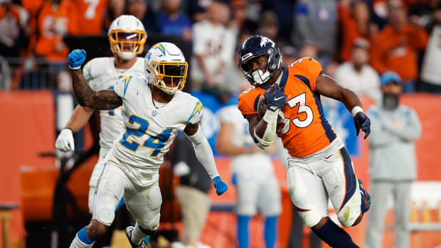 Denver Broncos running back Javonte Williams (33) runs the ball under pressure from Los Angeles Chargers safety Nasir Adderley (24) in the fourth quarter at Empower Field at Mile High.