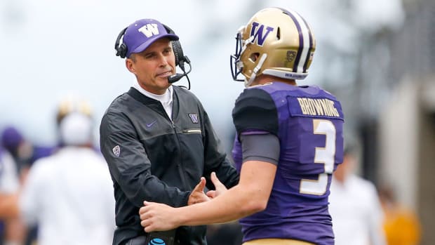 Washington coach Chris Petersen, who is wearing a headset and team hat, shakes hands with quarterback Jake Browning, who is in uniform.