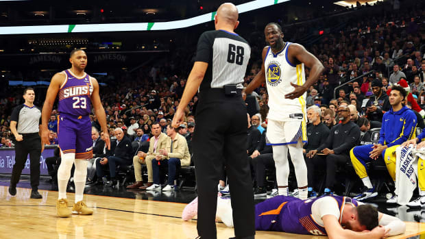 Warriors forward Draymond Green reacts to a call from an official while Suns center Jusuf Nurkić is on the ground with his head in his hands.