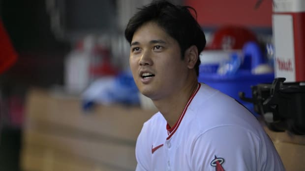 Angels star Shohei Ohtani looks up while speaking to someone in the dugout of a game.
