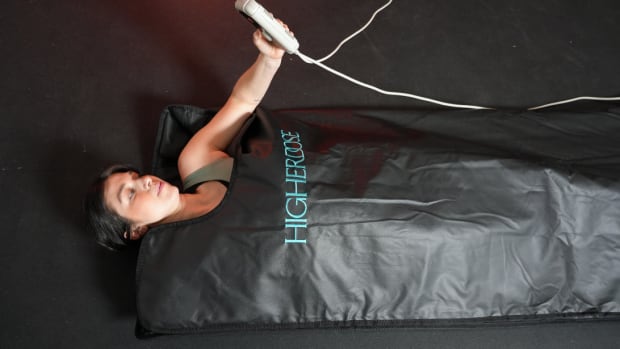 woman laying in Higherdose Infrared Sauna Blanket, holding controls