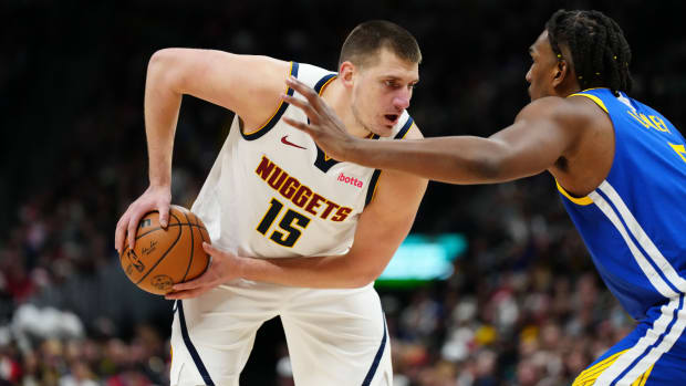 Nikola Jokic holds the basketball in two hands while Kevon Looney puts his arms out to defend