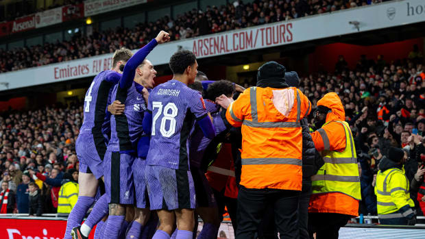 Liverpool's players pictured celebrating a goal during a 2-0 win at Arsenal in January 2024 while security staff at the Emirates Stadium attempt to remove a pitch invader from the field