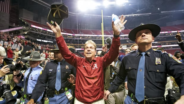 Nick Saban holds up his arms, while holding a hat and a water bottle after a game.