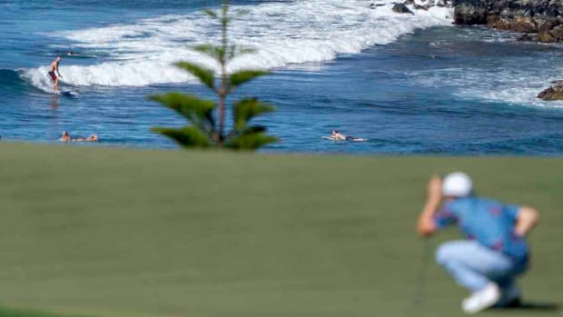 A surfer rides a wave as Matt Fitzpatrick lines up his putt on the 11th hole during the final round of the 2023 Sentry Tournament of Champions at Kapalua Resort.