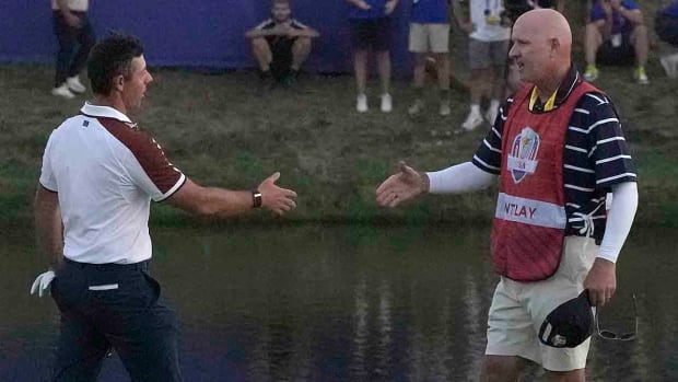 Rory McIlroy goes to shake hands with Patrick Cantlay's caddie Joe LaCava, on the 18th green following the end of during the afternoon Fourballs matches at the Ryder Cup golf tournament at the Marco Simone Golf Club in Guidonia Montecelio, Italy, Saturday, Sept. 30, 2023.