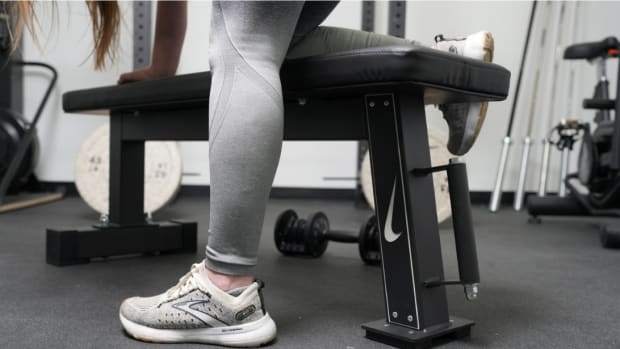 Lower half of a woman in grey leggings and grey shoes performing a row on the Nike rolling weight bench