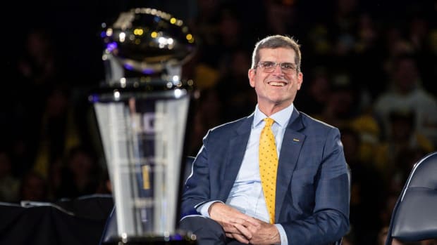 Michigan coach Jim Harbaugh looks at the program’s Big Ten championship trophy during a national title celebration.