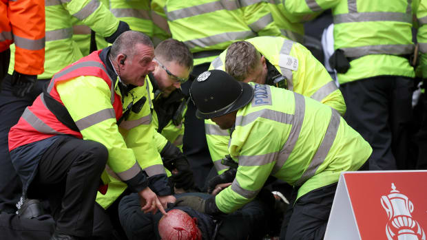 Police officers and a security steward pictured restraining an injured fan following crowd violence during an FA Cup game between West Brom and Wolves in January 2024