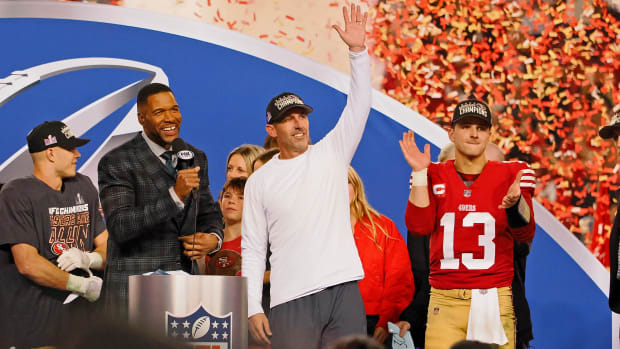 Christian McCaffrey, Michael Strahan, Kyle Shanahan and Brock Purdy all stand on stage celebrating as confetti falls around them