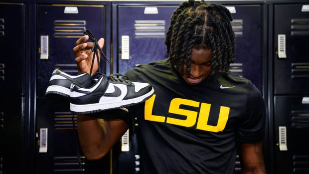 An LSU Tigers football player holds up black and white Nike Dunk sneakers.