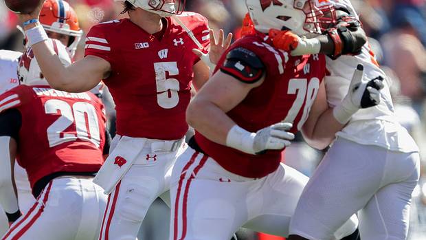Graham Mertz throwing the football against Illinois with a pass-rusher in his face.