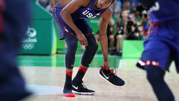 Team USA forward Kevin Durant picks up his shoe during a game.