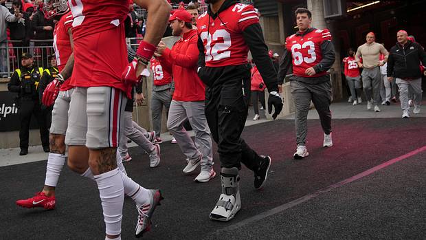 TreVeyon Henderson walks out of the tunnel in a walking boot.