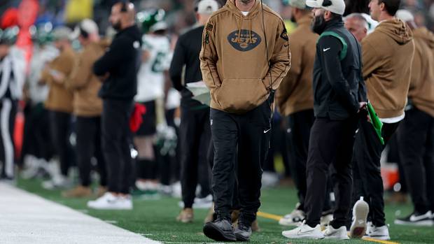 New York Jets injured quarterback Aaron Rodgers walks down the sidelines during a game.
